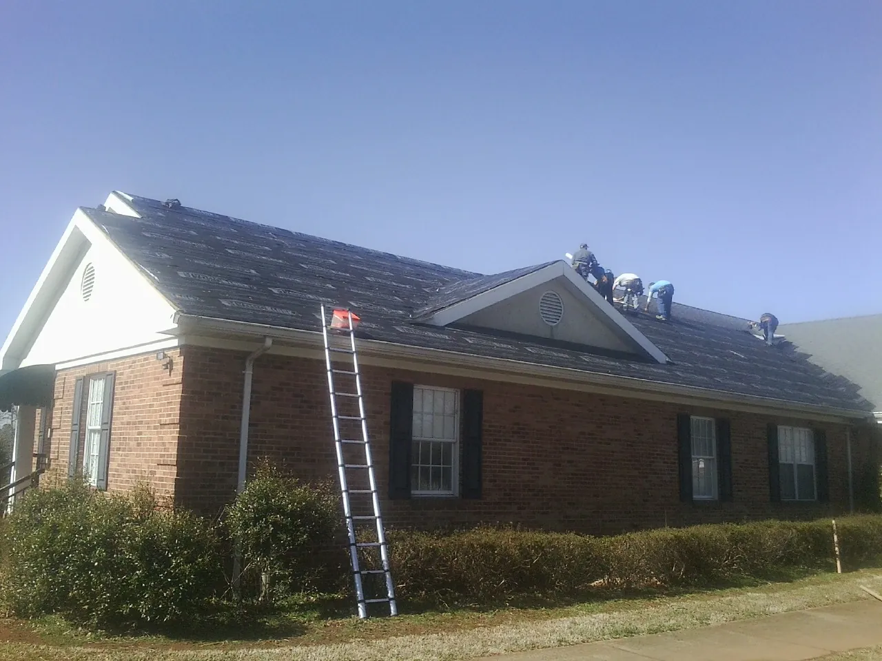 Crew tearing shingles off a brick ranch roof with a ladder set — Emergency Roof Repair work by our crew in Quinebaug