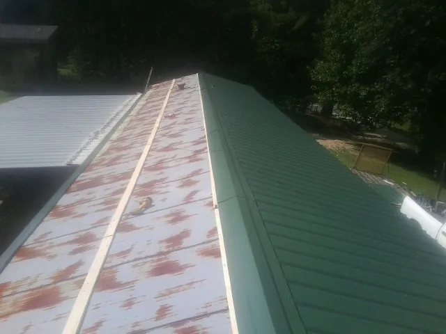 Old rusted panels beside newly installed green metal roofing — Wind Damage Roof Repair by Roofing Brothers in Quinebaug