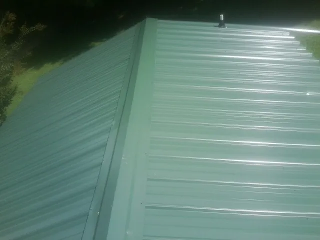 New green metal panels meeting at the ridge of a roof — Flat Roof Repair work by our crew in Quinebaug
