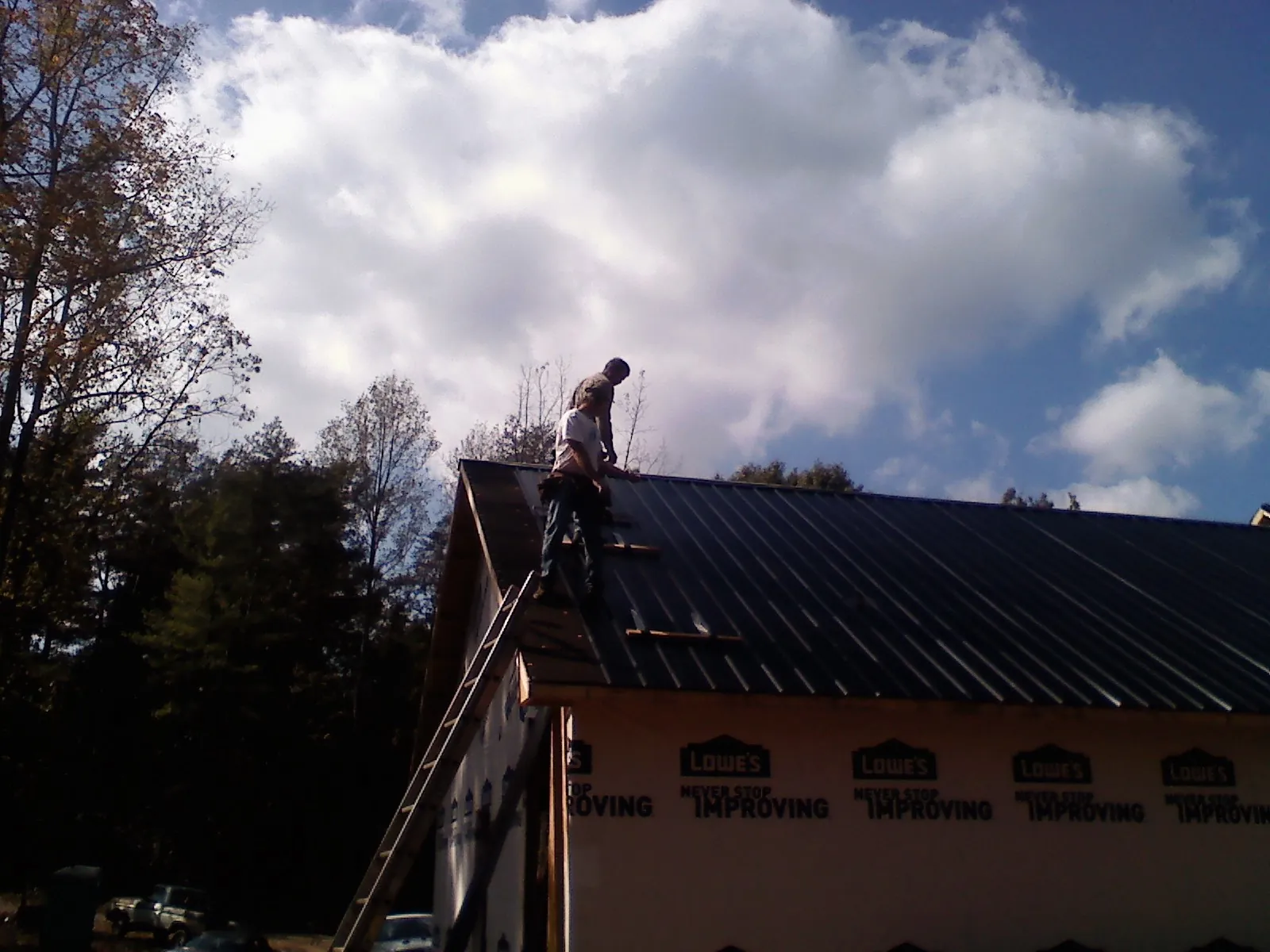 Roofer fastening dark metal panels high against a cloudy sky, from a Roof Inspection job in Quinebaug