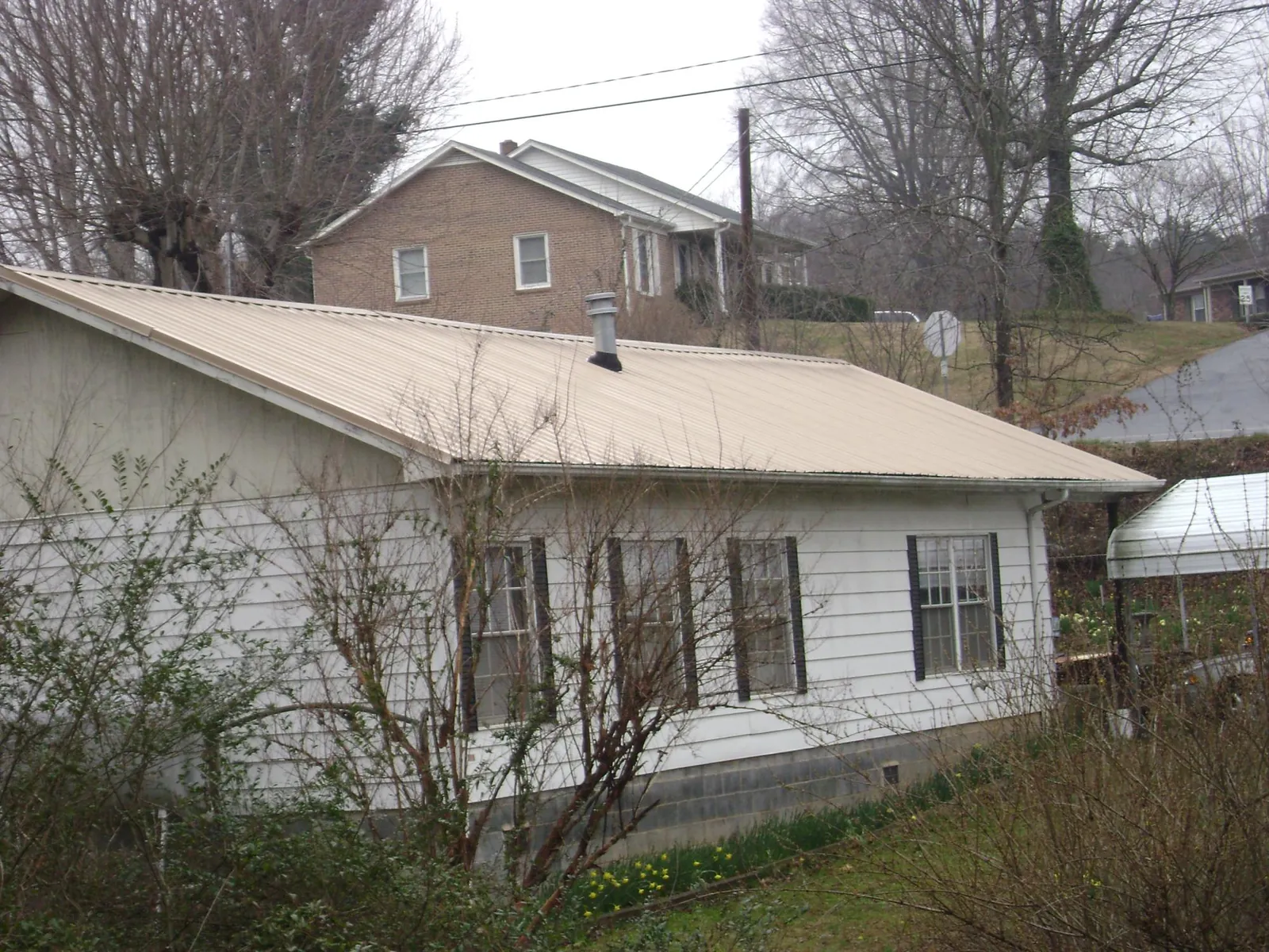 Tan metal roof on a white sided house set into a hillside — Commercial Roofing by Roofing Brothers in Quinebaug