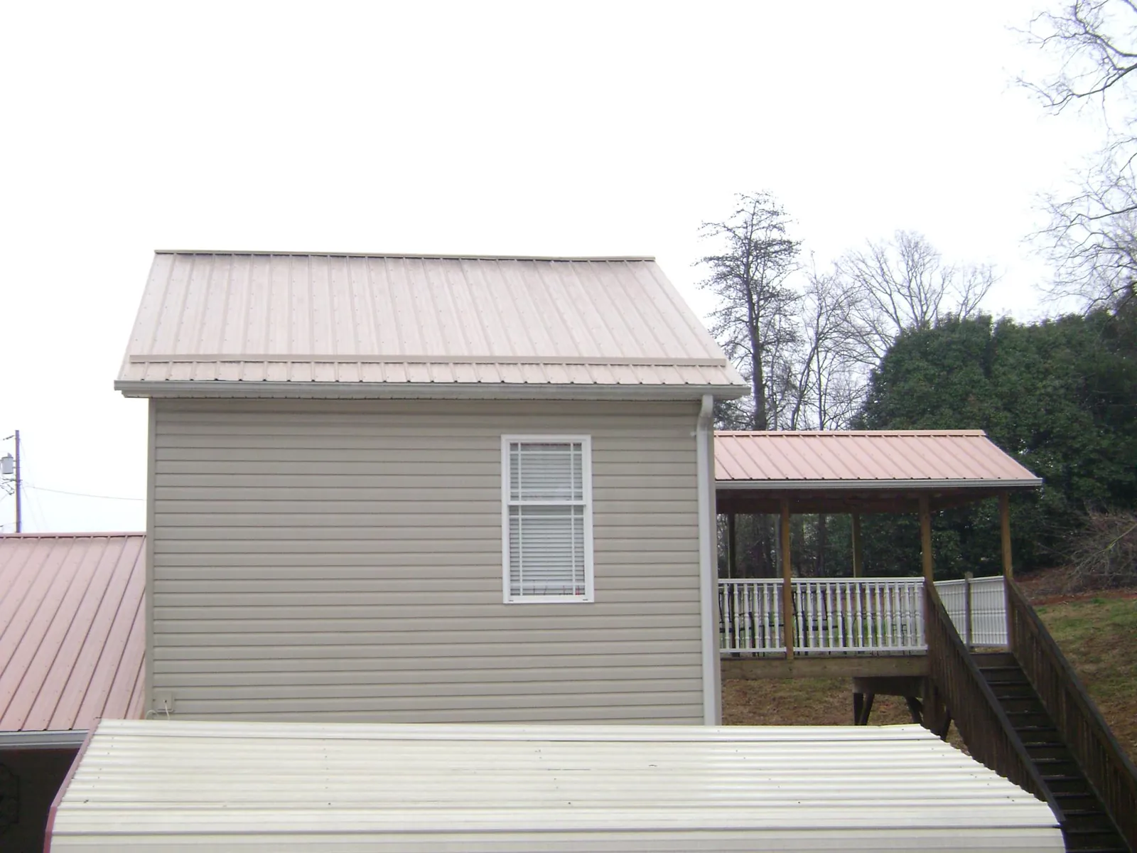 Tan metal roofs on a two story addition and attached porch, from a Roof Replacement job in Quinebaug